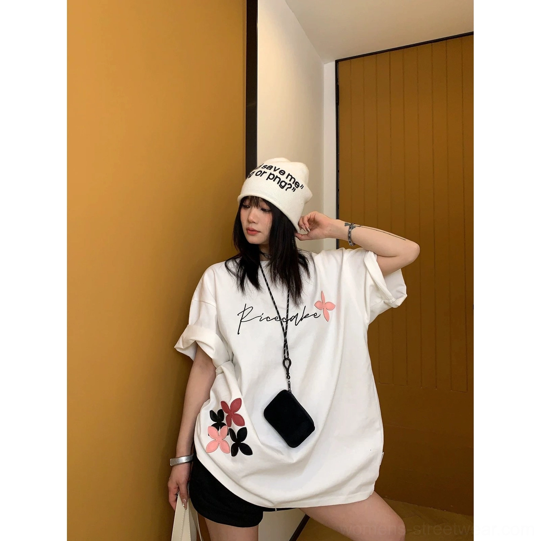 White oversized script floral streetwear T-shirt styled with black shorts, a white beanie, and a casual crossbody bag