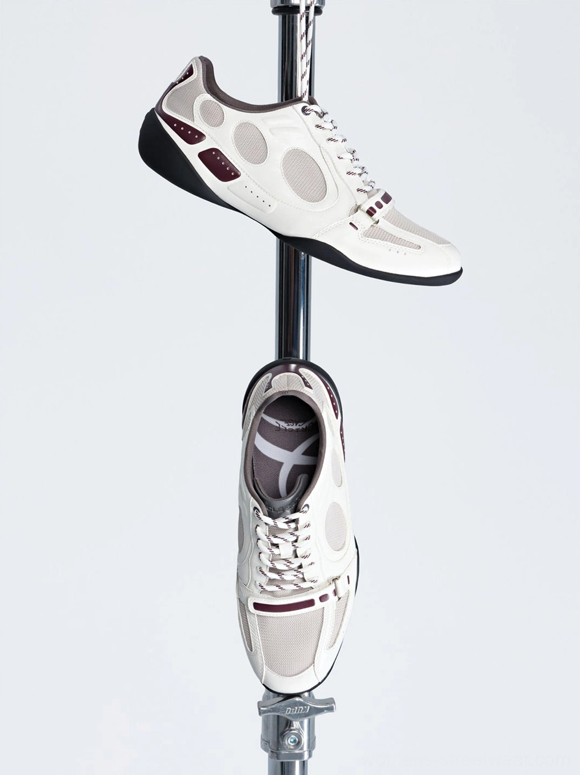 White perforated retro sport sneakers displayed on a metal rack showing perforated side panels and burgundy accents