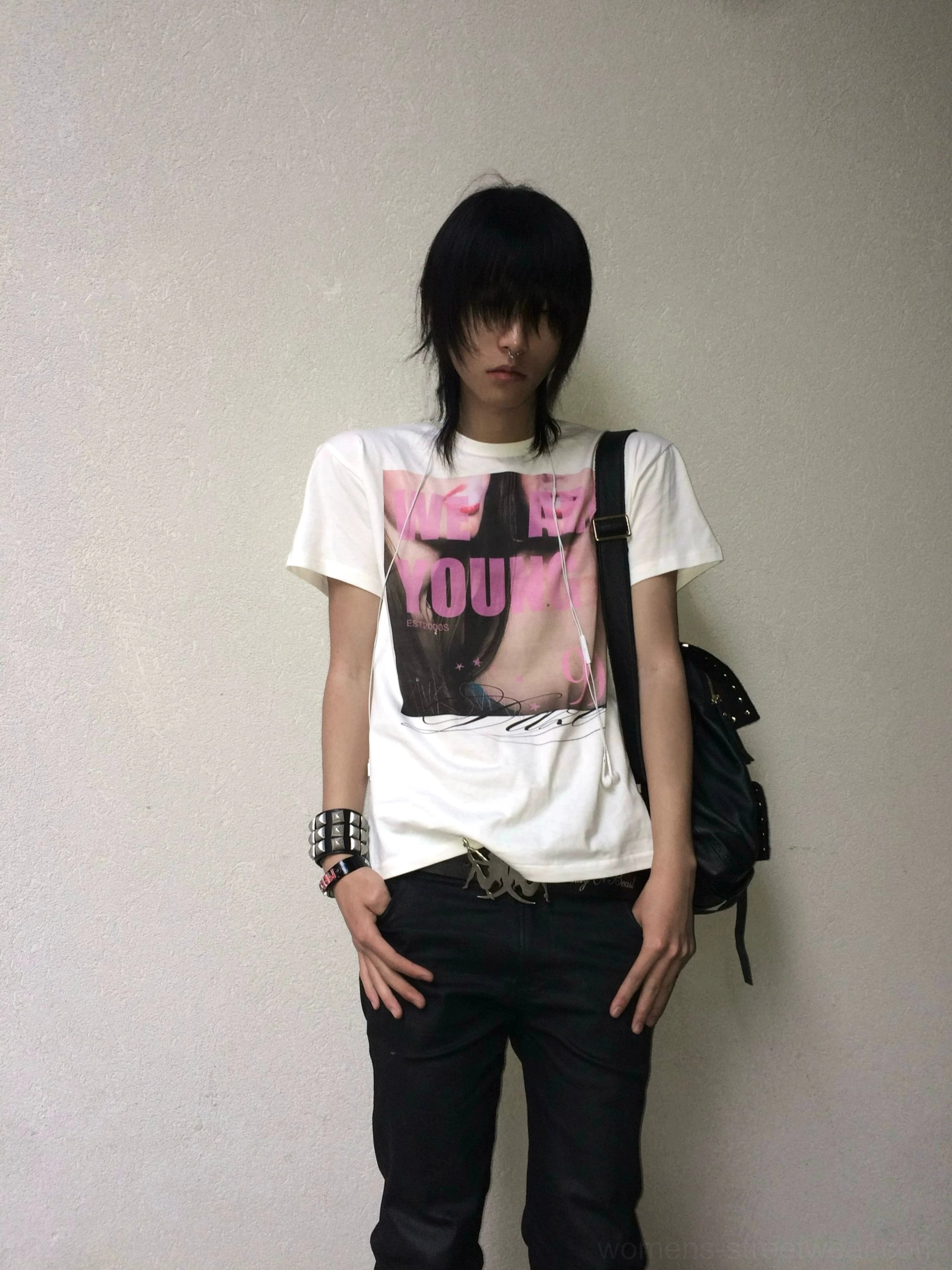 Full-body streetwear outfit featuring a white pink graphic T-shirt with portrait print, black pants, backpack, and studded bracelet