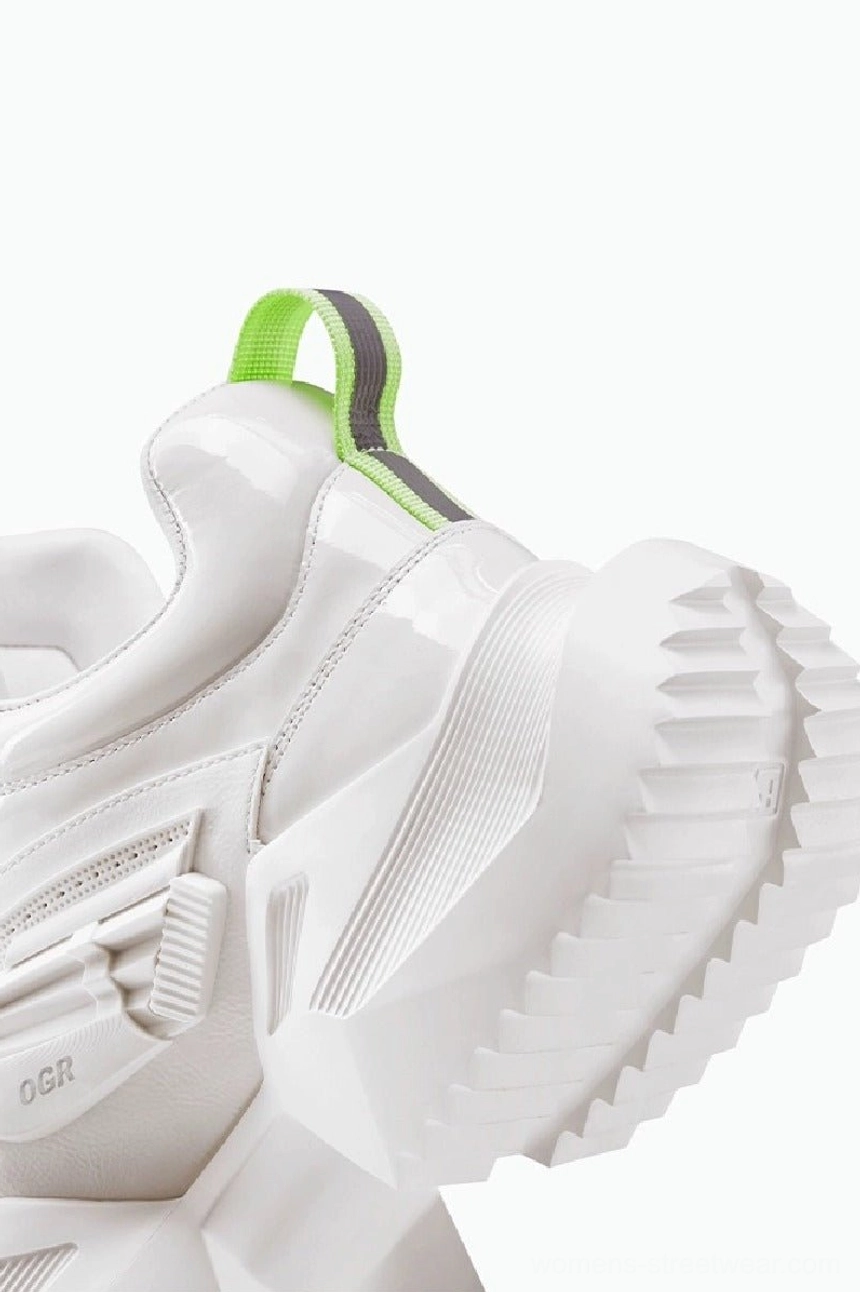 Rear oblique close-up of a white platform sneaker showing the bright neon reflective heel pull tab, sculpted jagged outsole, and dimensional futuristic construction