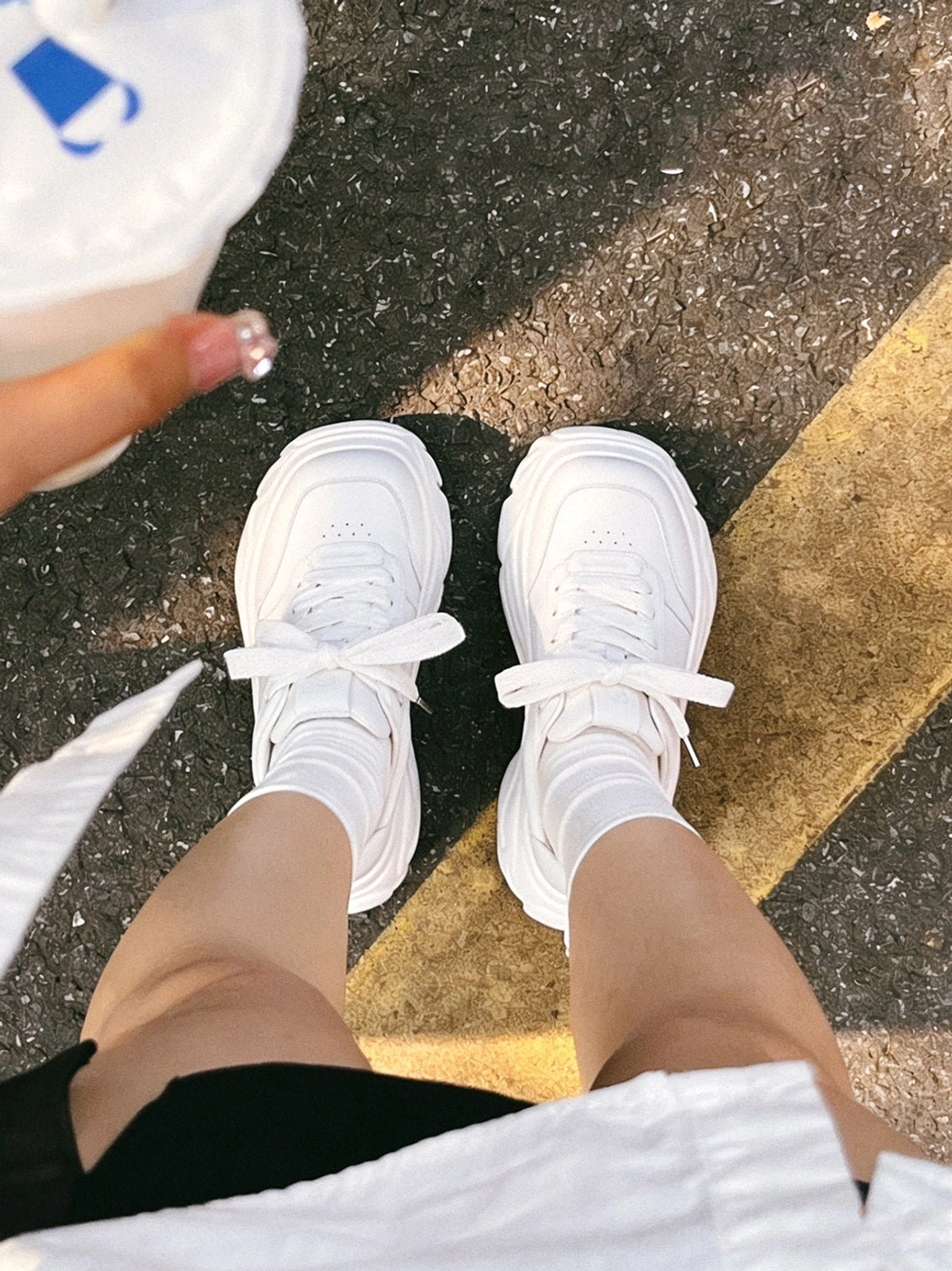 White platform sneakers worn with white crew socks on an urban asphalt road for a clean monochrome streetwear outfit