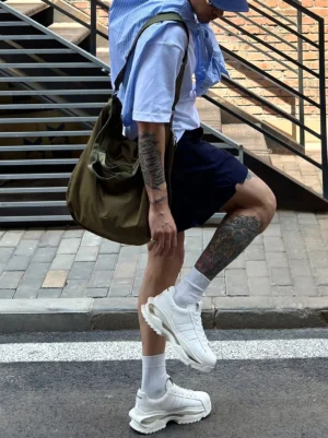 White platform sneakers worn by a male streetwear model on an urban stairway, highlighting the chunky cutout sole and all-white low-top silhouette