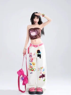 Front full-body view of white playful graffiti wide-leg jeans with colorful cartoon prints, pink waist belt, and plush waist charm in a minimalist streetwear studio
