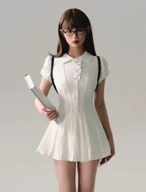 White pleated Peter Pan collar mini shirt dress shown in a full front view with fitted waist puff sleeves ruffled button placket and flared pleated skirt