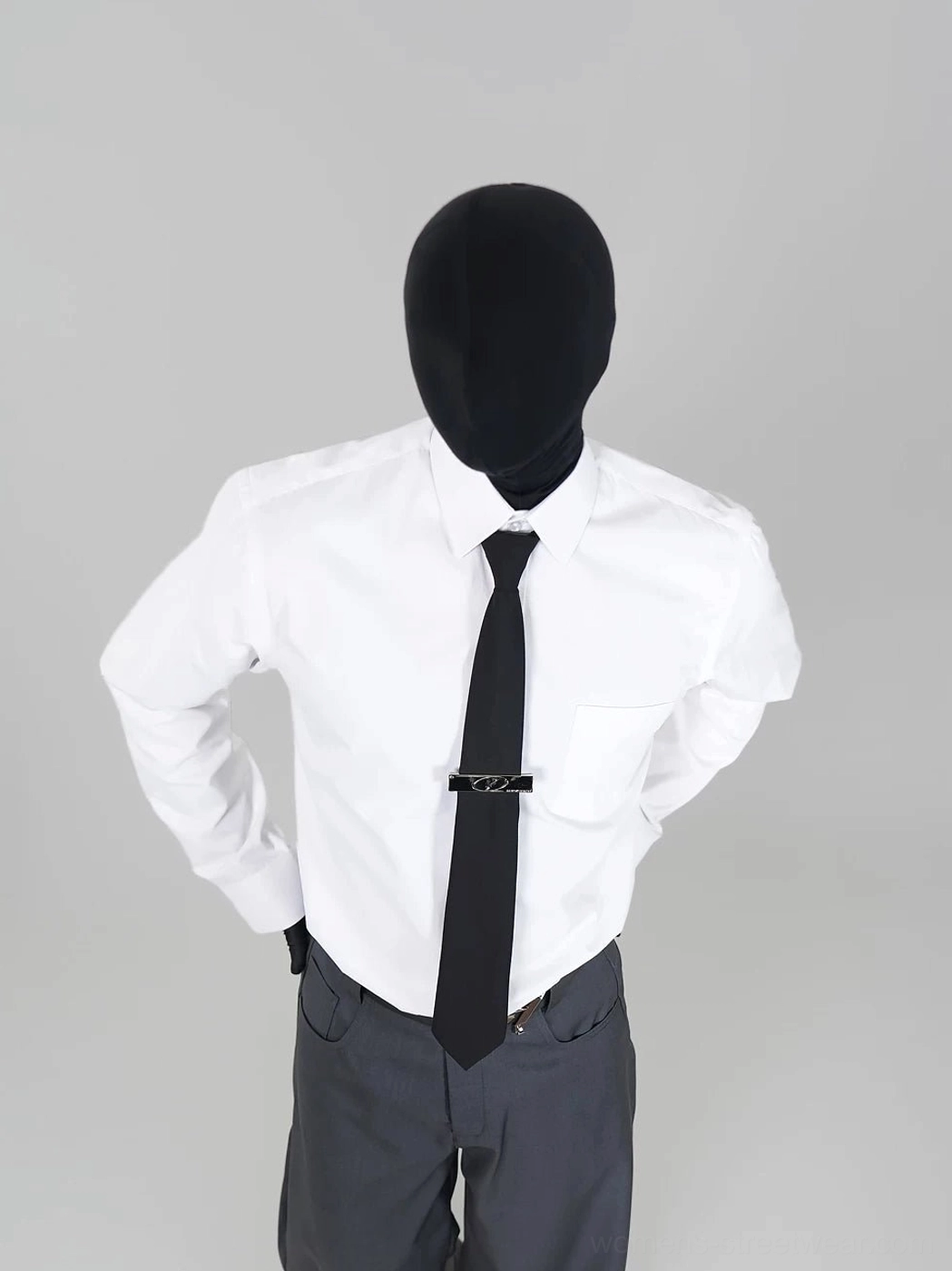 White point-collar long-sleeve streetwear shirt styled with a silver tie clip and tailored gray trousers in a minimalist studio