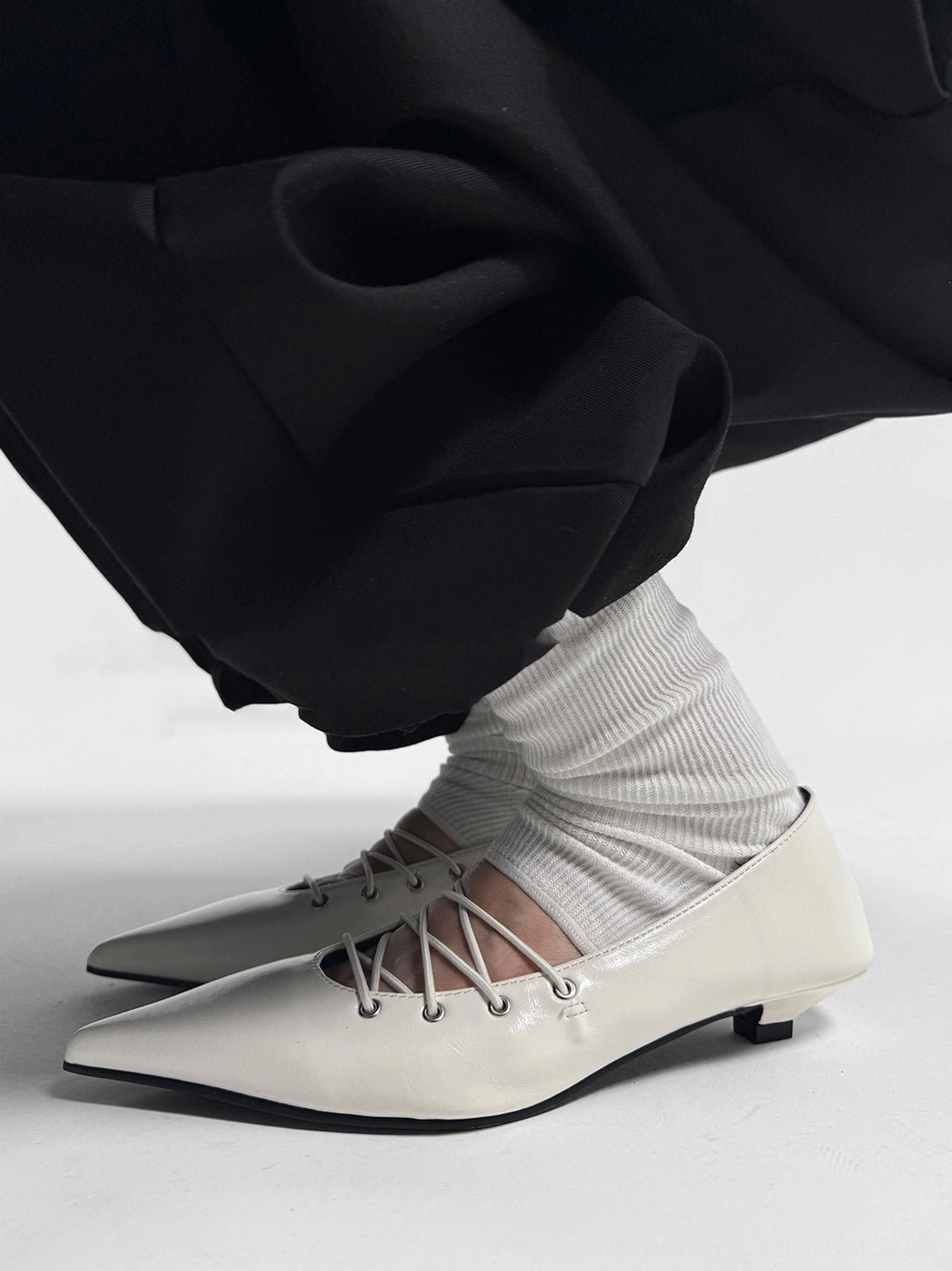 Side view of white pointed ballet flats with glossy leather-look finish, small block heel, black outsole, and corset-style laces