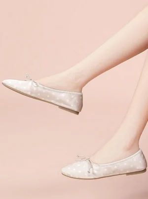 Woman wearing white polka dot bow ballet flats against a soft pink background, showing the fitted Y2K ballet-core styling