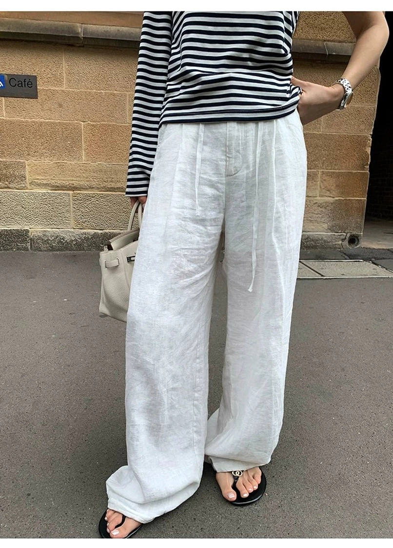 White ramie linen wide leg pants close-up overhead flat lay view, drawstring waist with black slide sandals and crepe texture detail