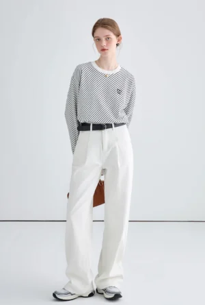 Full-body front view of white relaxed wide-leg jeans styled with a striped crew-neck top, black belt, tan handbag, and casual sneakers