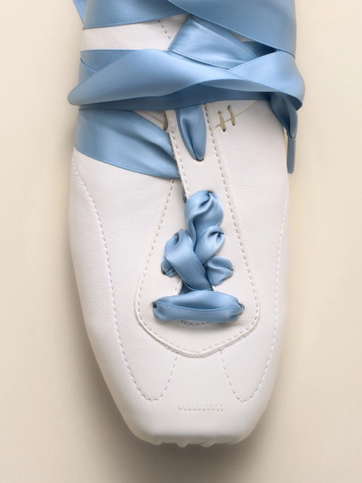 White low-profile retro trainers with sky blue satin ribbon laces tied into decorative bows and visible stitched detailing