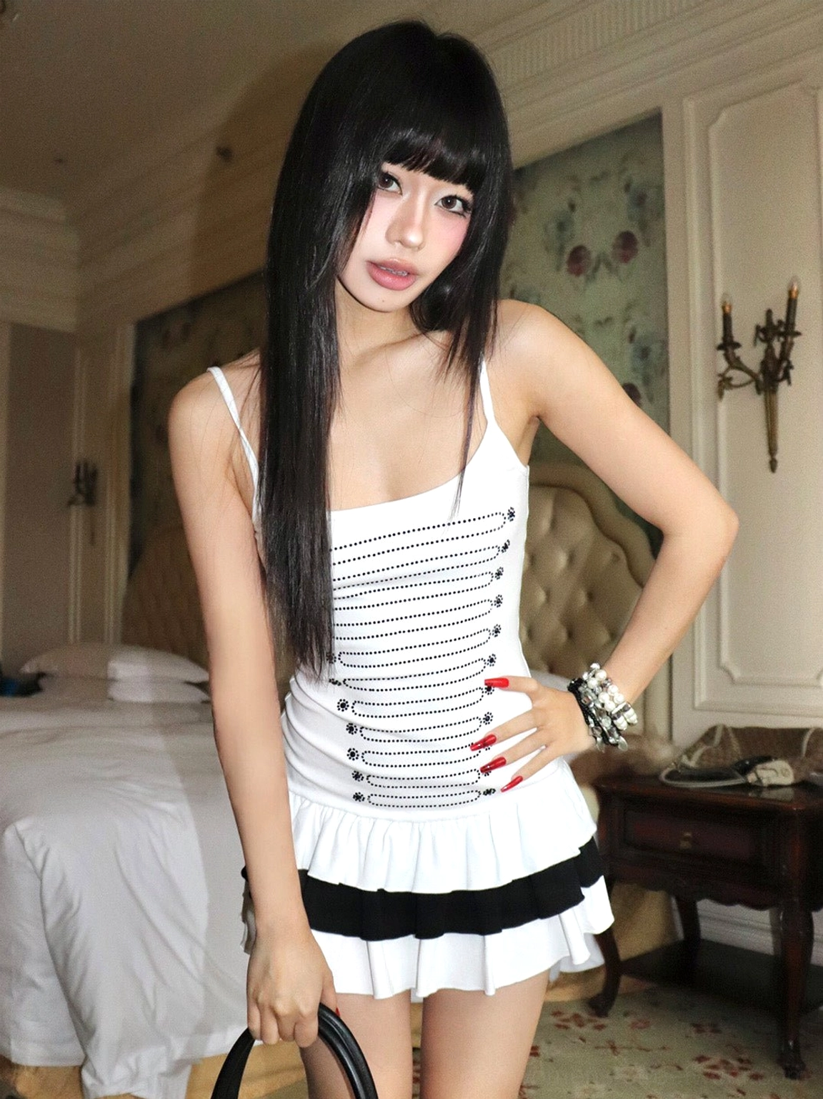 Model wearing a white rhinestone tiered mini dress with black ruffled hem in a luxury hotel bedroom