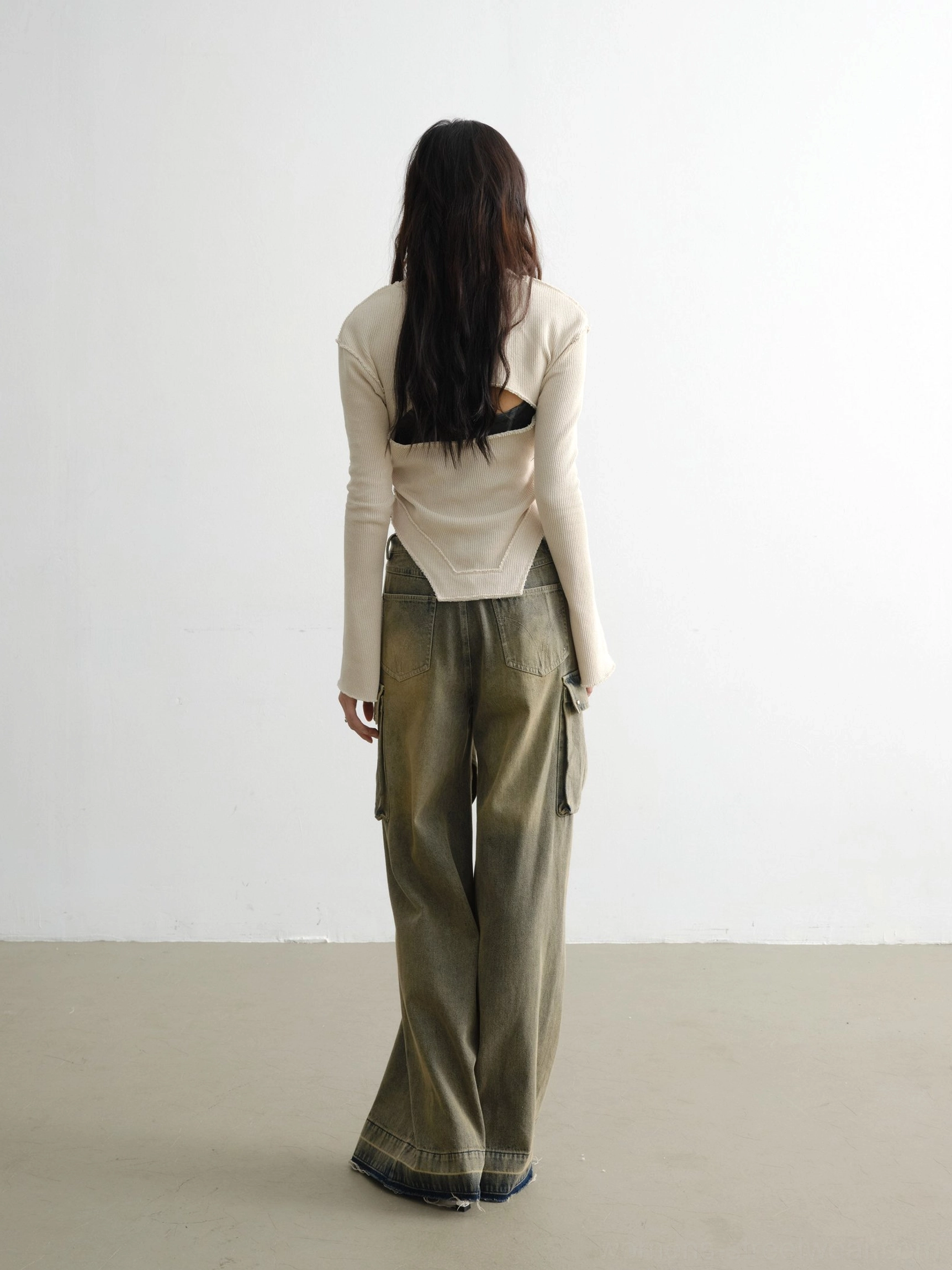 Back view of white ribbed knit streetwear top featuring a subtle back cutout and asymmetric hem with vintage wide-leg cargo jeans