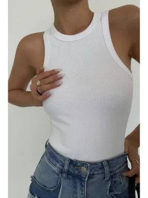 Close-up chest detail of white ribbed knit tank top showing fabric texture, paired with blue denim jeans, partial model view
