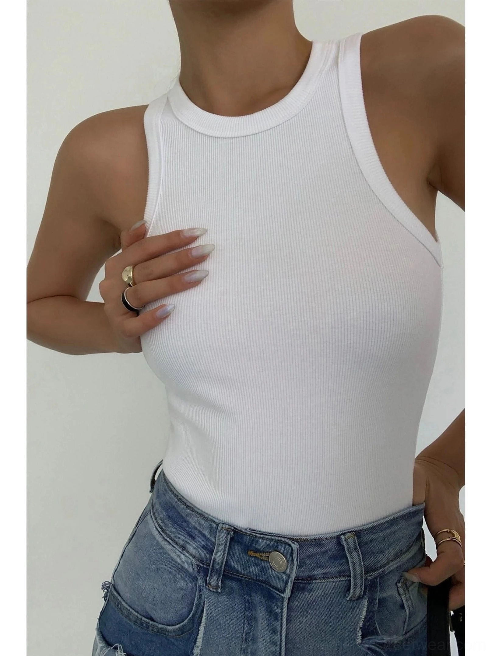 Close-up chest detail of white ribbed knit tank top showing fabric texture, paired with blue denim jeans, partial model view