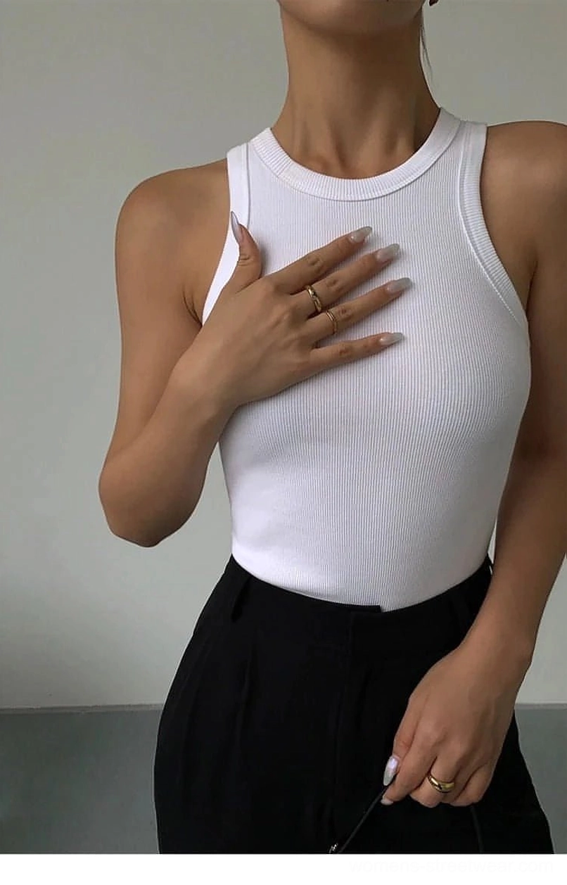 Close-up detail shot of white ribbed knit tank top fabric and neckline on female model, paired with black suit pants, texture and construction focus