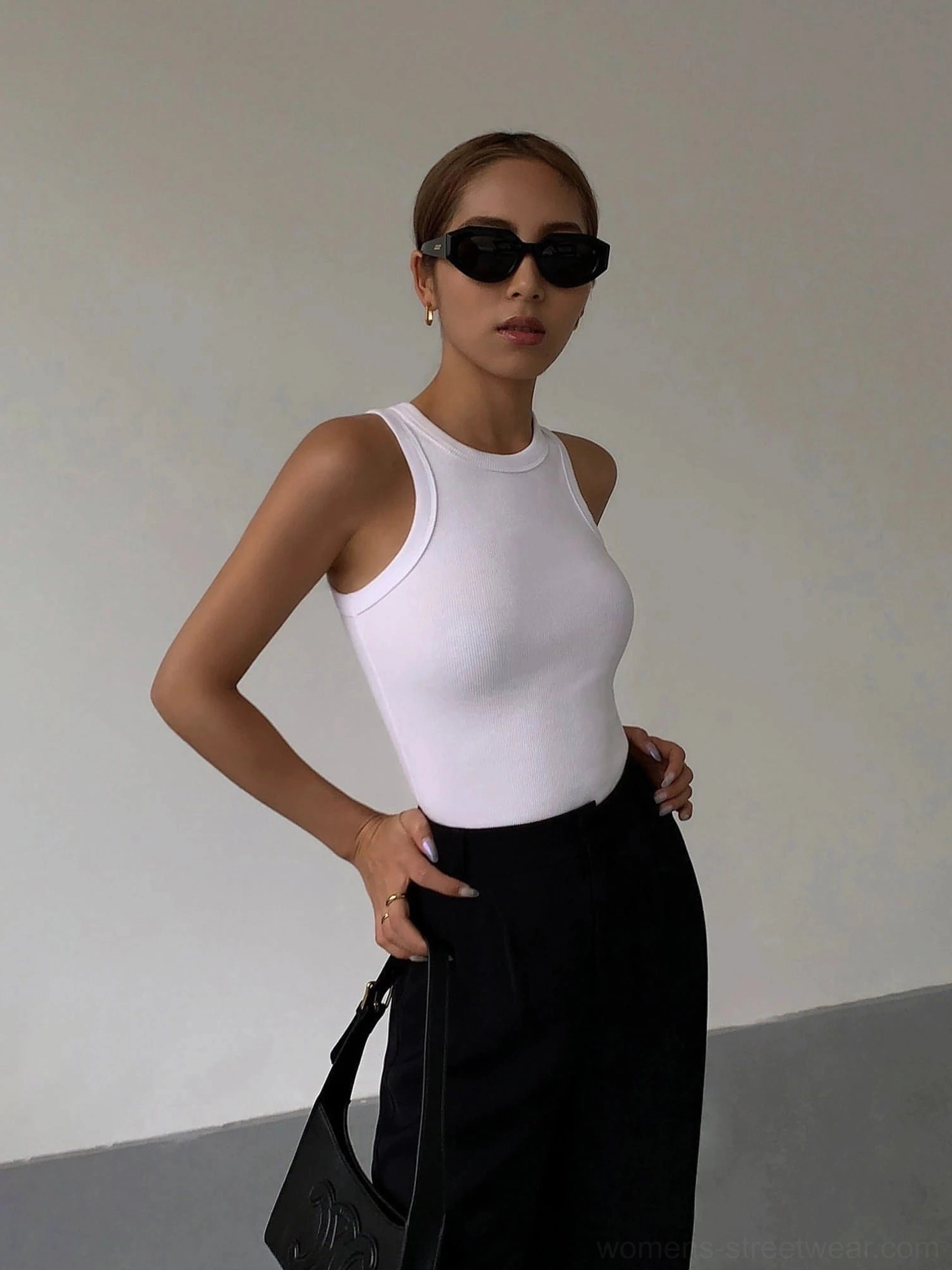 White ribbed knit tank top worn with black suit pants and black handbag, front half-body view on female model wearing black sunglasses, minimalist studio background