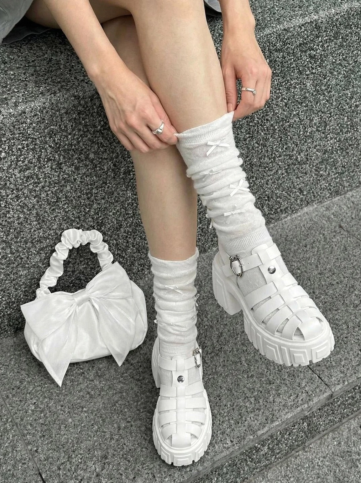 Overhead view of white Roman platform sandals with heart ankle buckles, chunky lug soles, bow socks, and a white handbag