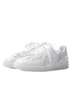 Front three-quarter view of white rose low-top sneakers with glossy synthetic leather uppers, satin ribbon laces, embroidered detailing, 3D white flower decoration, and translucent rubber soles