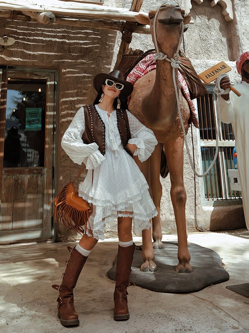 White ruffle midi dress layered with a western leather vest and fringe crossbody bag for a relaxed cowboy streetwear outfit