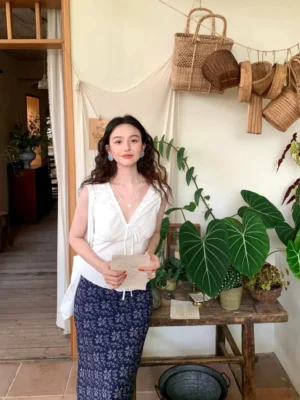 White ruffle tie-front sleeveless wrap blouse styled with a navy floral midi skirt in a vintage cottagecore interior