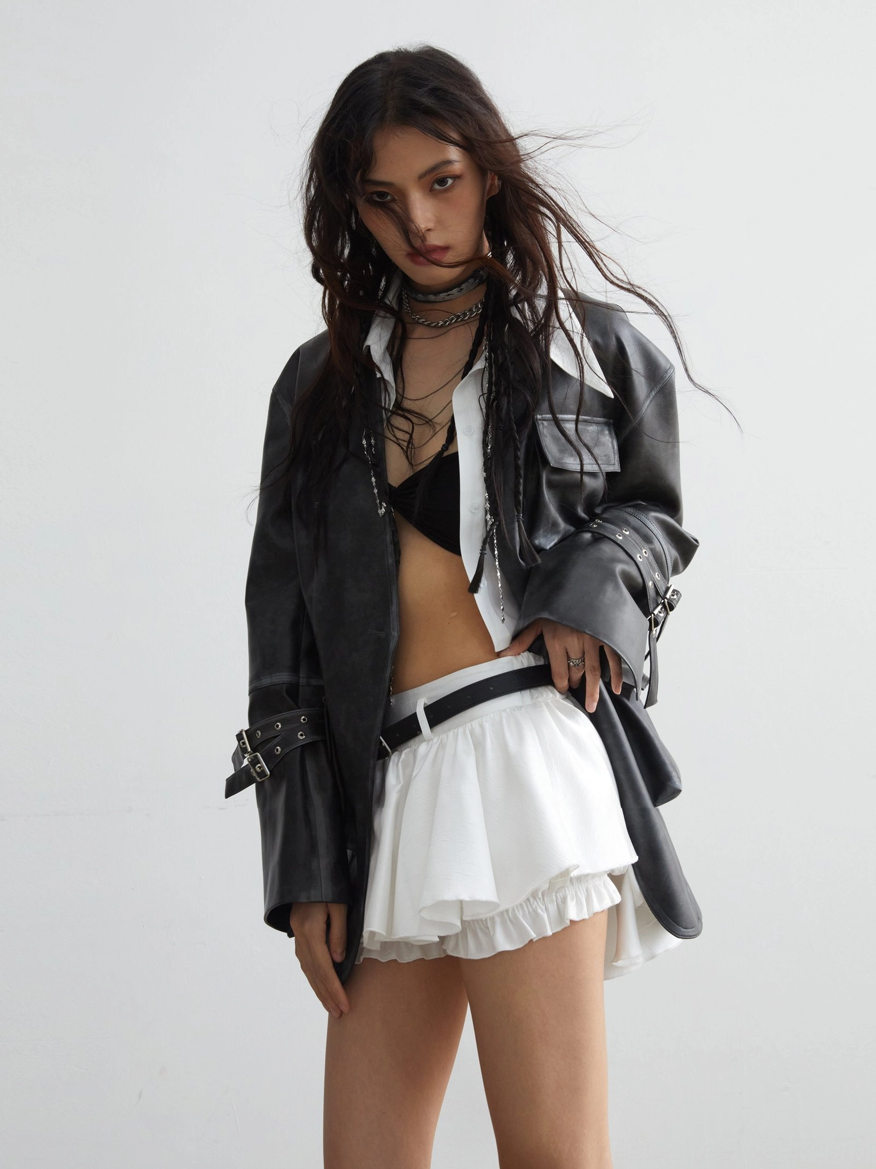 Korean streetwear outfit featuring white high waisted ruffled mini skirt black belt and oversized leather jacket