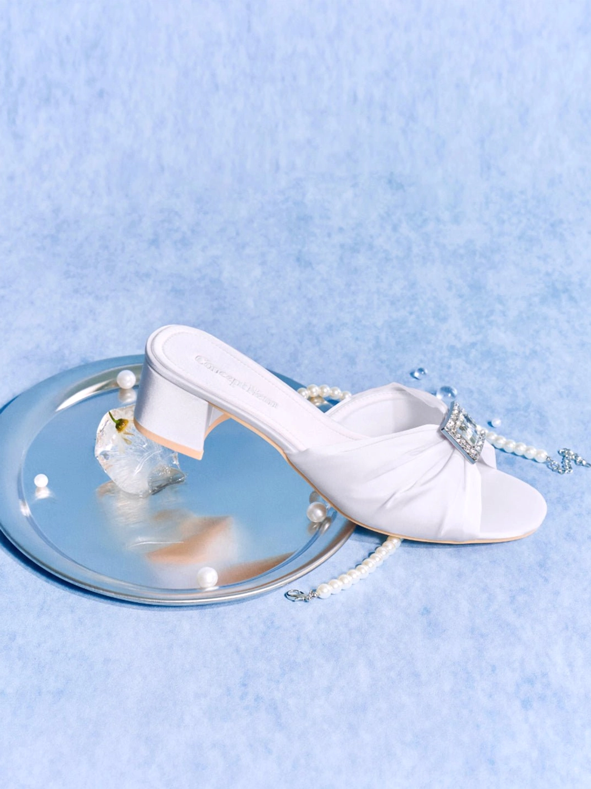 White satin crystal-buckle mule slides displayed from above with ruched upper and pearl chain decoration