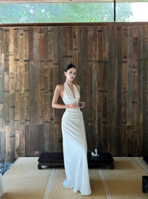 Front full-body view of a white satin halter backless maxi dress with deep V neckline, corset-inspired waist seams, and flowing floor-length silhouette