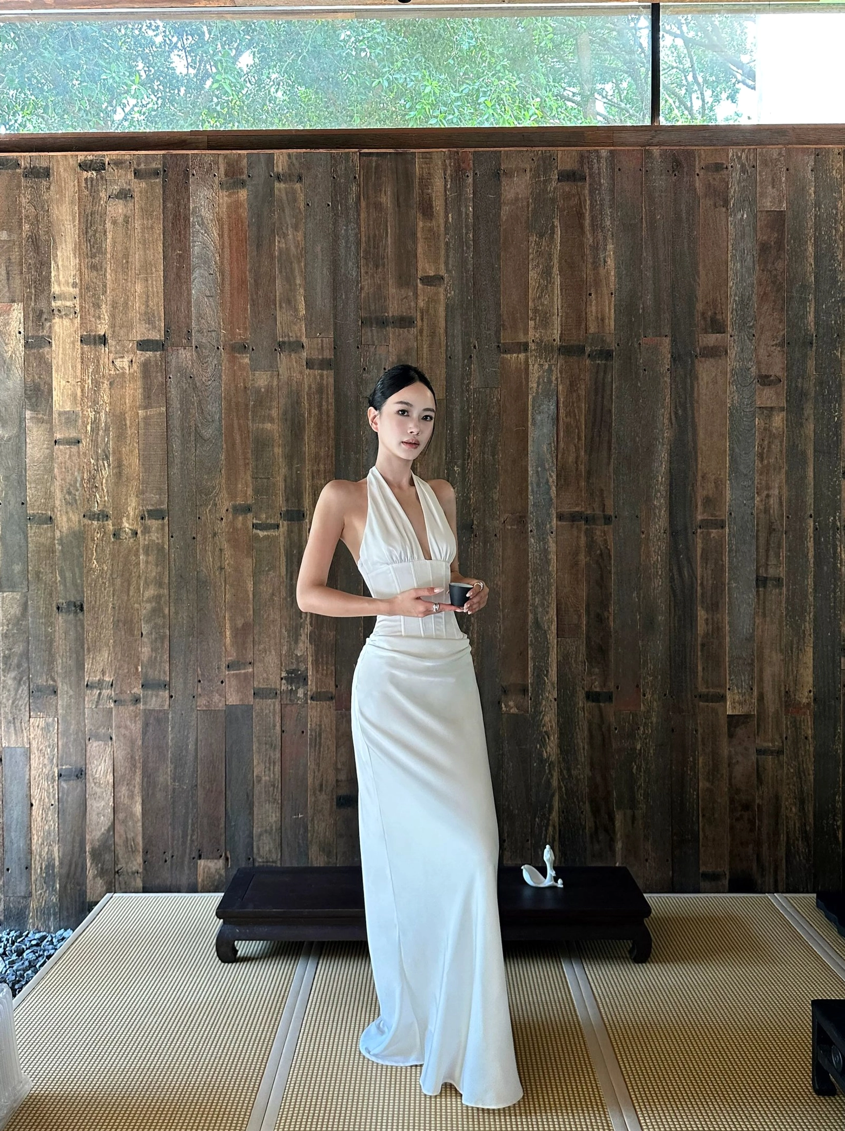 Front full-body view of a white satin halter backless maxi dress with deep V neckline, corset-inspired waist seams, and flowing floor-length silhouette