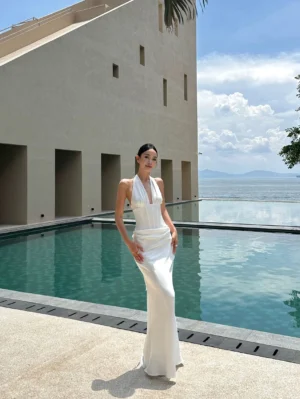 White satin halter maxi dress styled beside a minimalist poolside villa, showing the fitted corset bodice and sleek mermaid floor-length hem