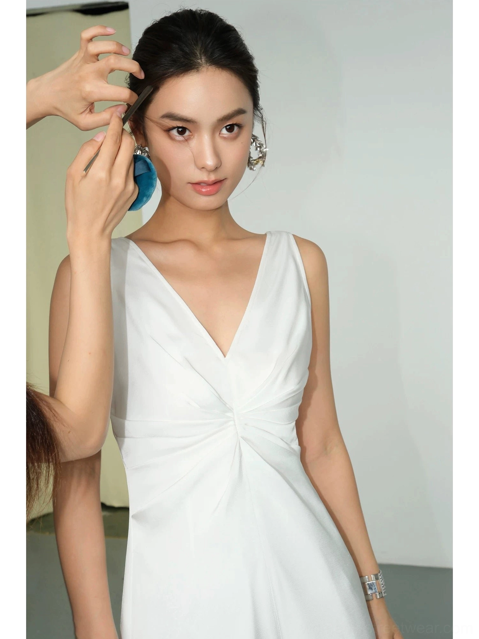 White satin twist-front maxi dress close-up with V-neckline, sculptural ruched bust detail, sleeveless silhouette and elegant accessories