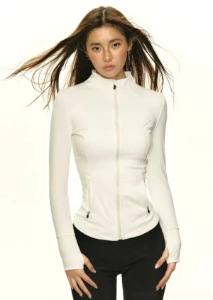 Female model wearing a fitted white mock neck zip-up athletic streetwear jacket with black pants