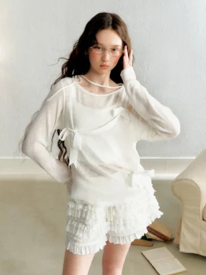 White sheer long sleeve bow wrap top styled with layered ruffled shorts in a soft indoor streetwear fashion look