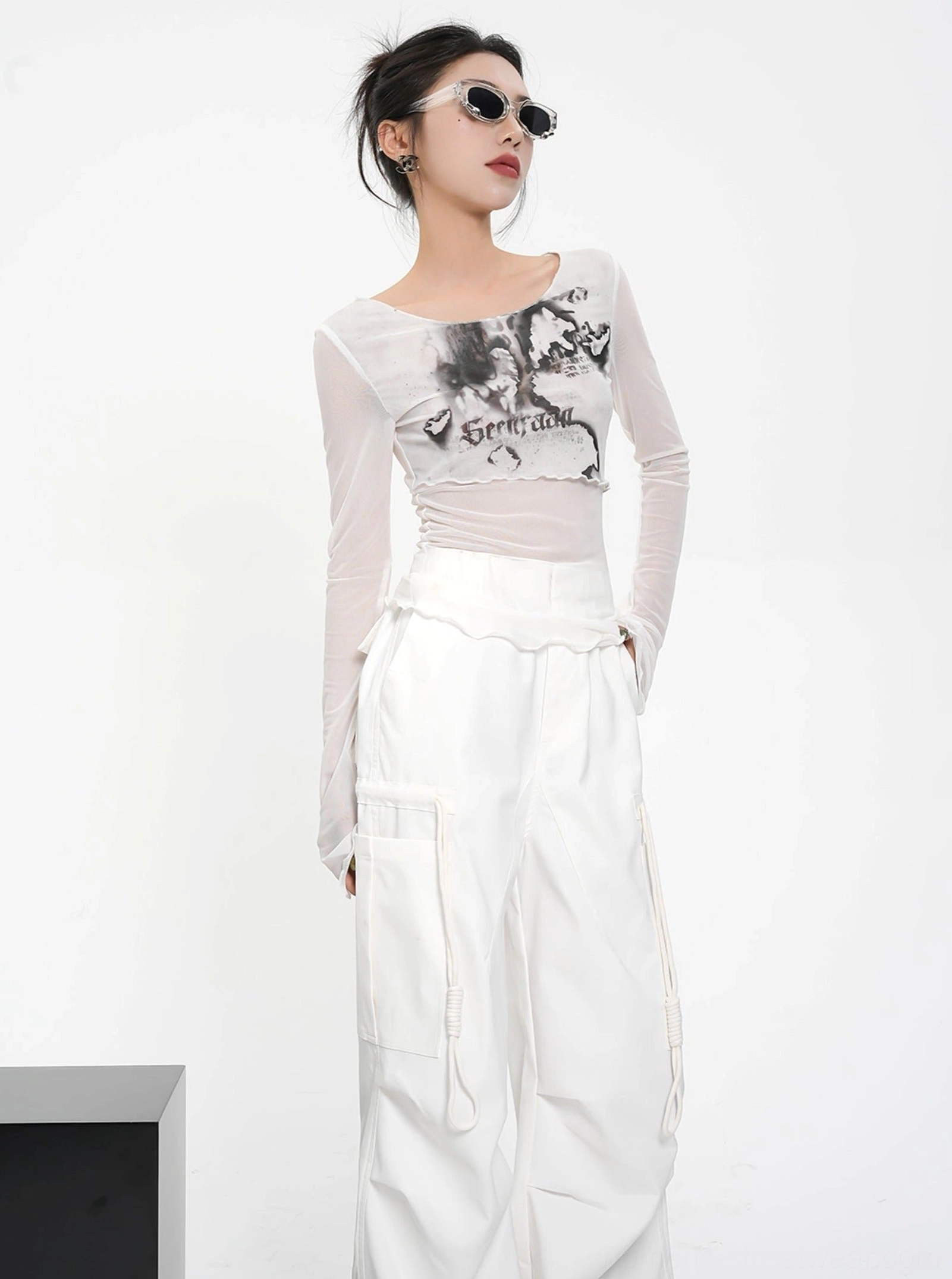 Three-quarter view of a white sheer mesh floral graphic crop top with long sleeves and asymmetrical neckline