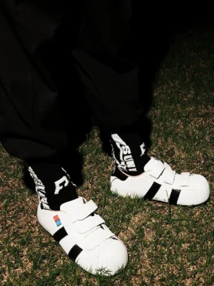 White shell toe hidden lift sneakers with hook-and-loop straps styled with black streetwear pants and graphic socks outdoors