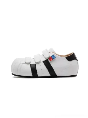 White shell toe strap sneakers with black side stripes and concealed 3 cm hidden lift on a plain background