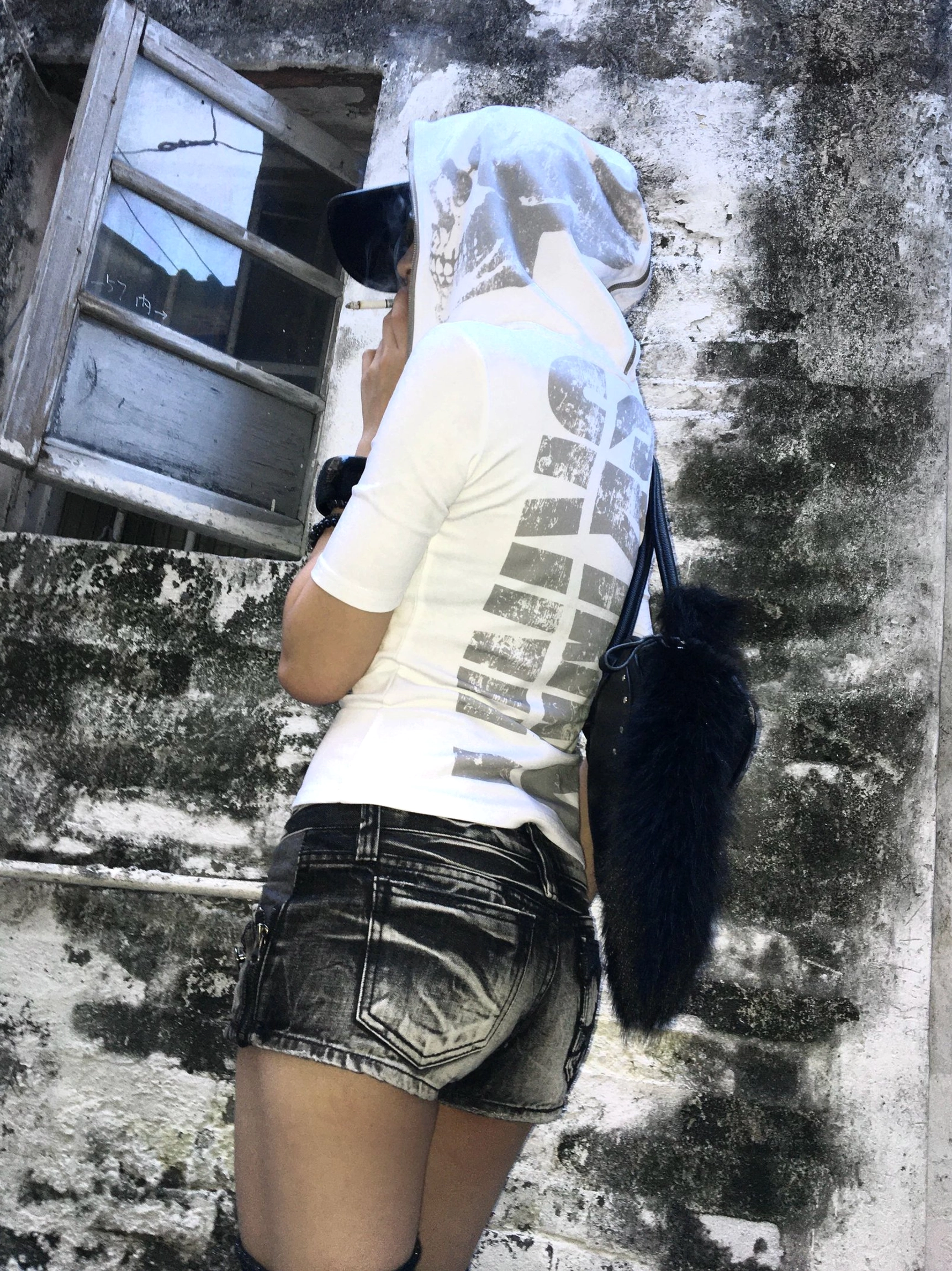 Back three-quarter view of a white hooded graphic tee featuring a bold grey vertical print styled with distressed denim shorts