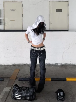 Front full-body view of a woman wearing a white fitted hooded half-sleeve streetwear tee with a cropped silhouette in an industrial parking lot
