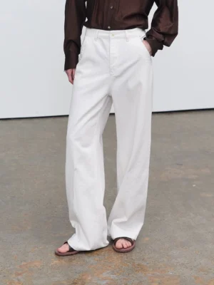 Front low-angle view of white slub-textured relaxed straight-leg jeans with a high waist, long stacked hem, and minimalist streetwear styling