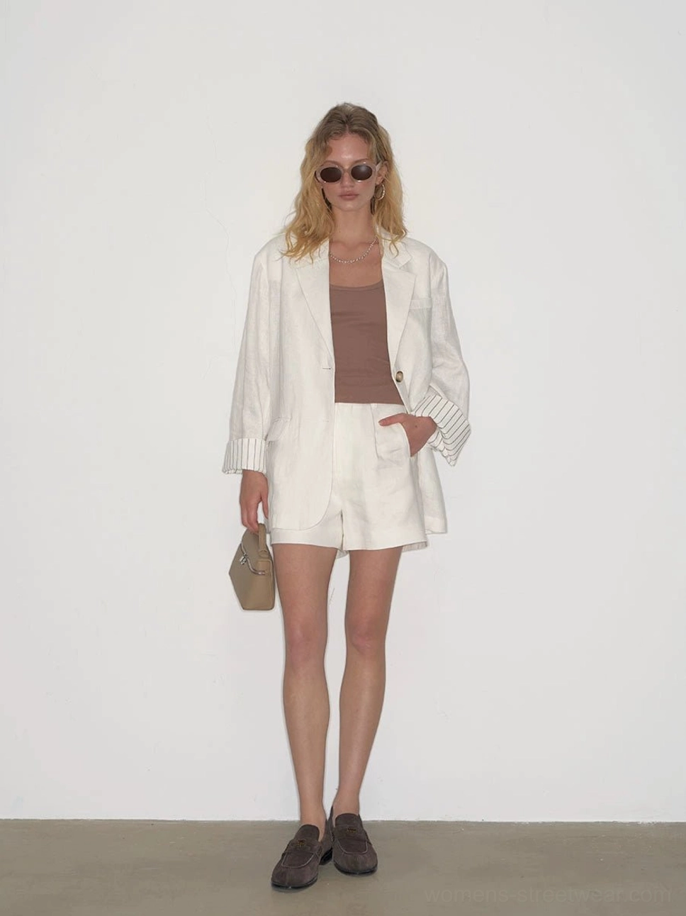 Full-length view of white tailored pleated shorts paired with a matching blazer, beige handbag, and brown leather loafers in a minimalist Seoul-inspired outfit