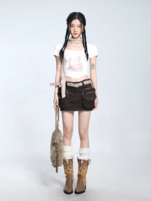 White fitted teacup bunny graphic cropped T-shirt with curved hem styled with brown cargo mini skirt, leather belt, cowboy boots, and furry tote