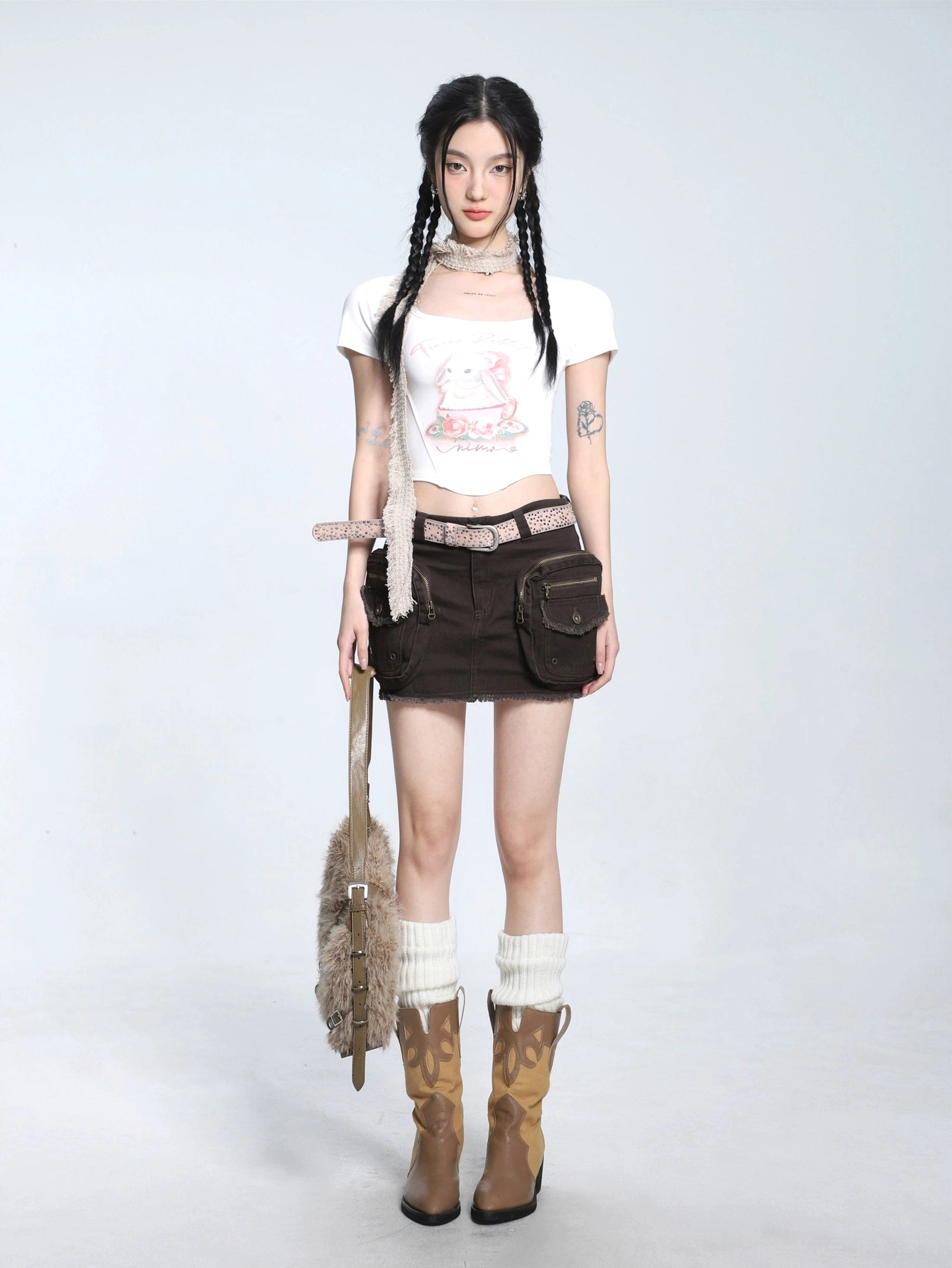 White fitted teacup bunny graphic cropped T-shirt with curved hem styled with brown cargo mini skirt, leather belt, cowboy boots, and furry tote