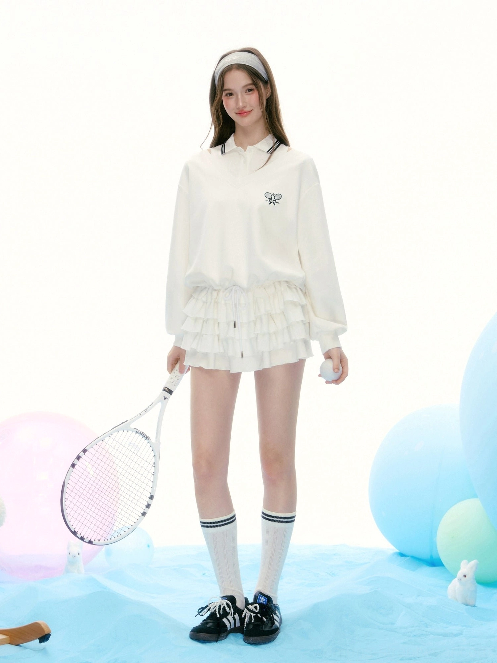 Full body model wearing a white tennis streetwear polo and layered ruffle skirt set with sporty socks and sneakers