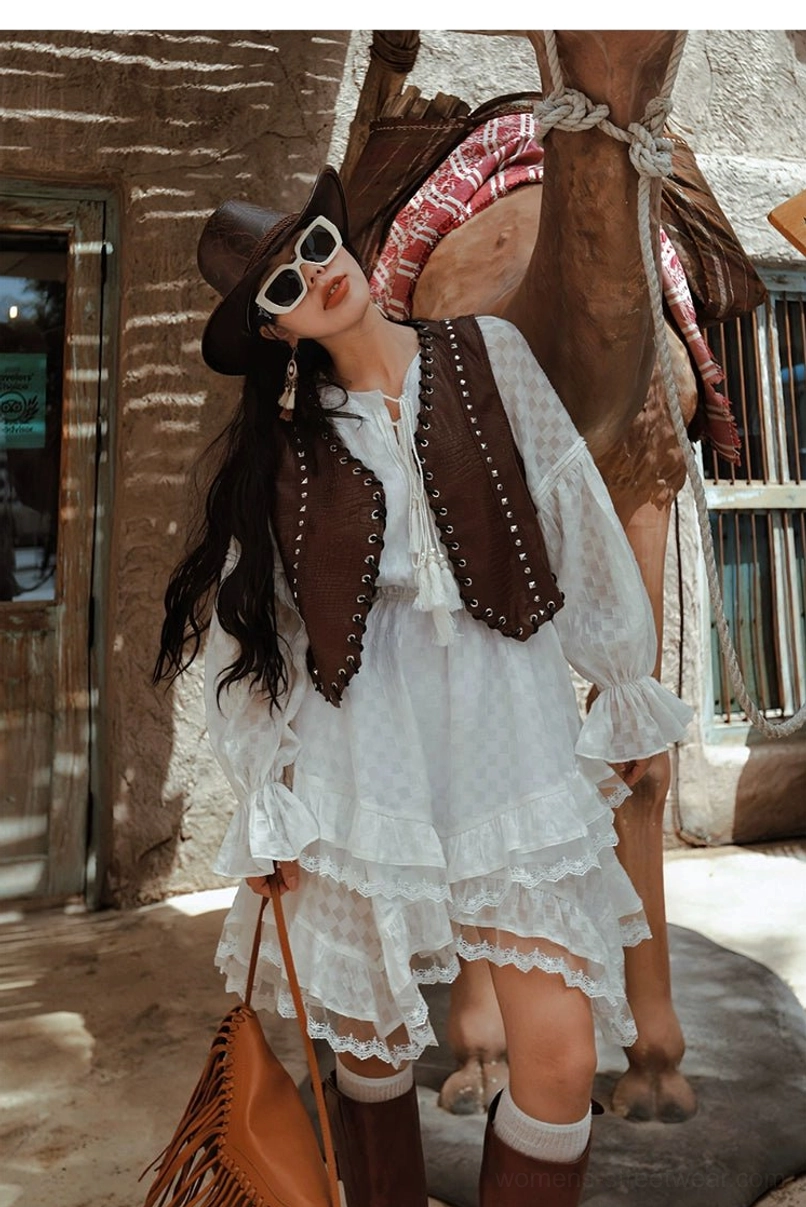 White tiered ruffle midi dress styled with a studded brown leather vest and western accessories beside a camel