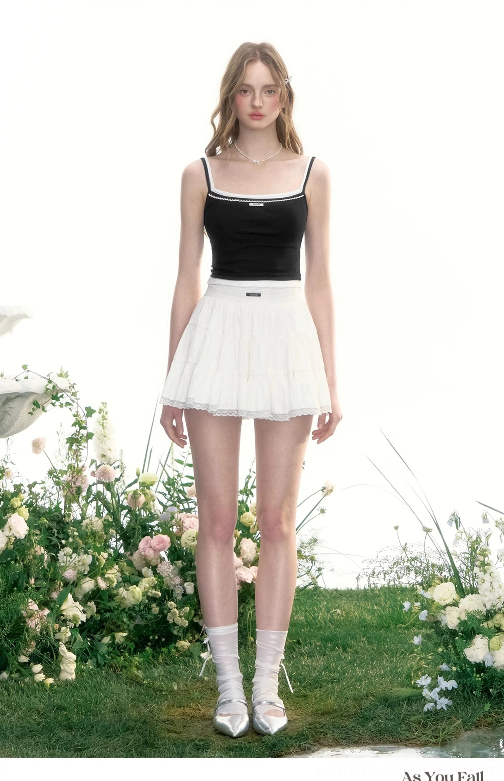 White tiered tennis skirt styled with a black camisole, white socks, and silver loafers in minimalist streetwear