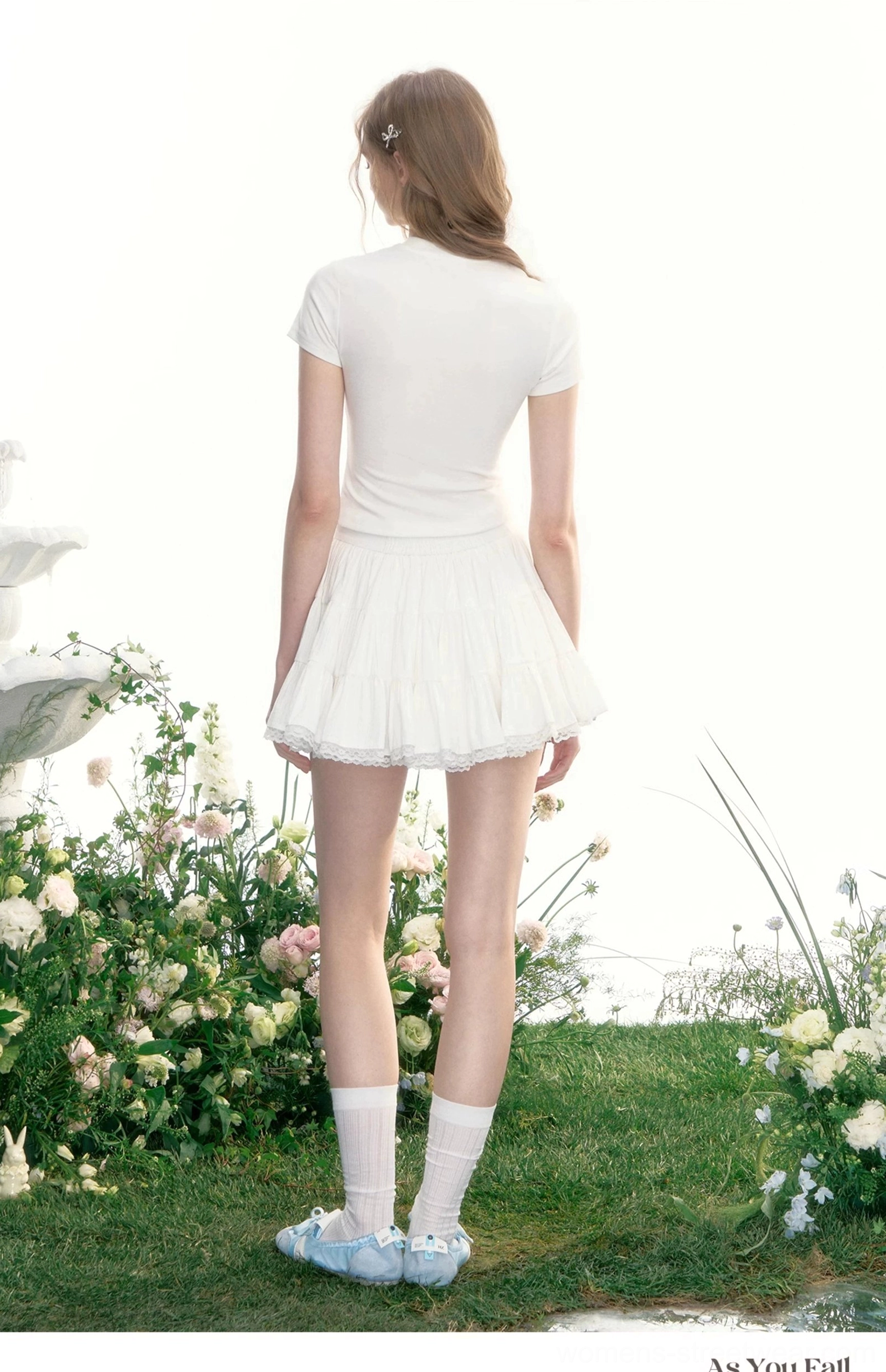 Back view of a white flowy tiered tennis mini skirt styled with white socks and blue loafers