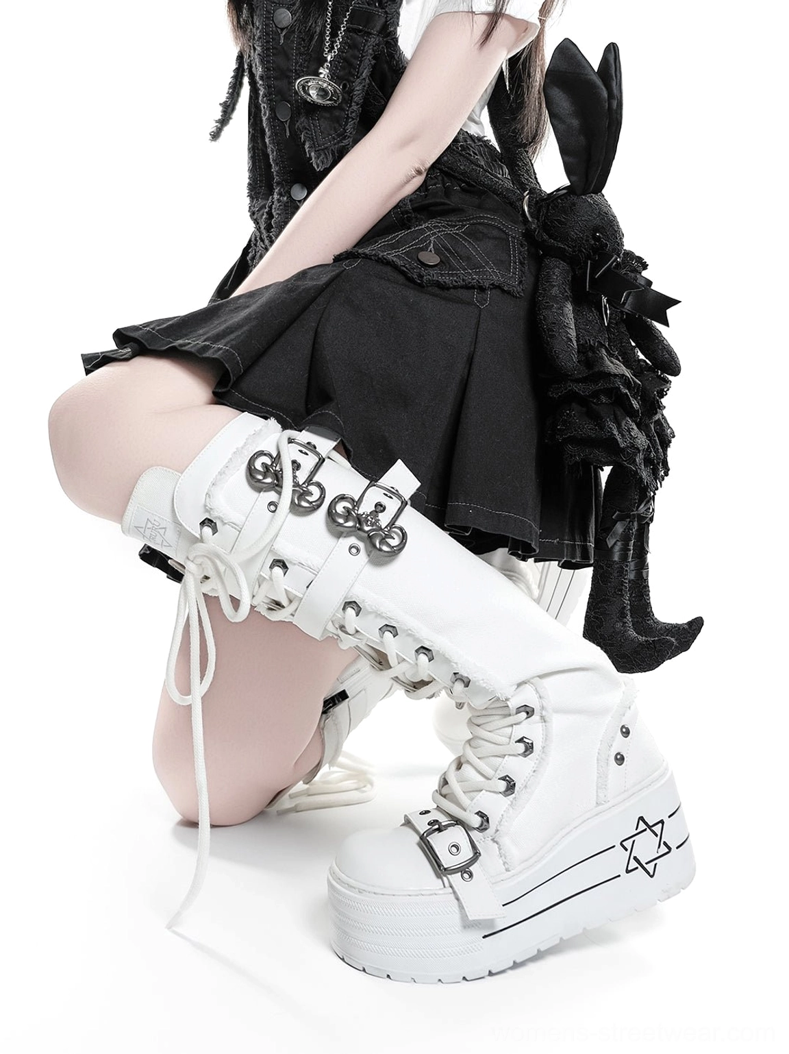 Close-up of white triple-buckle knee-high platform combat boots showing metal straps and hexagram-style sole graphic