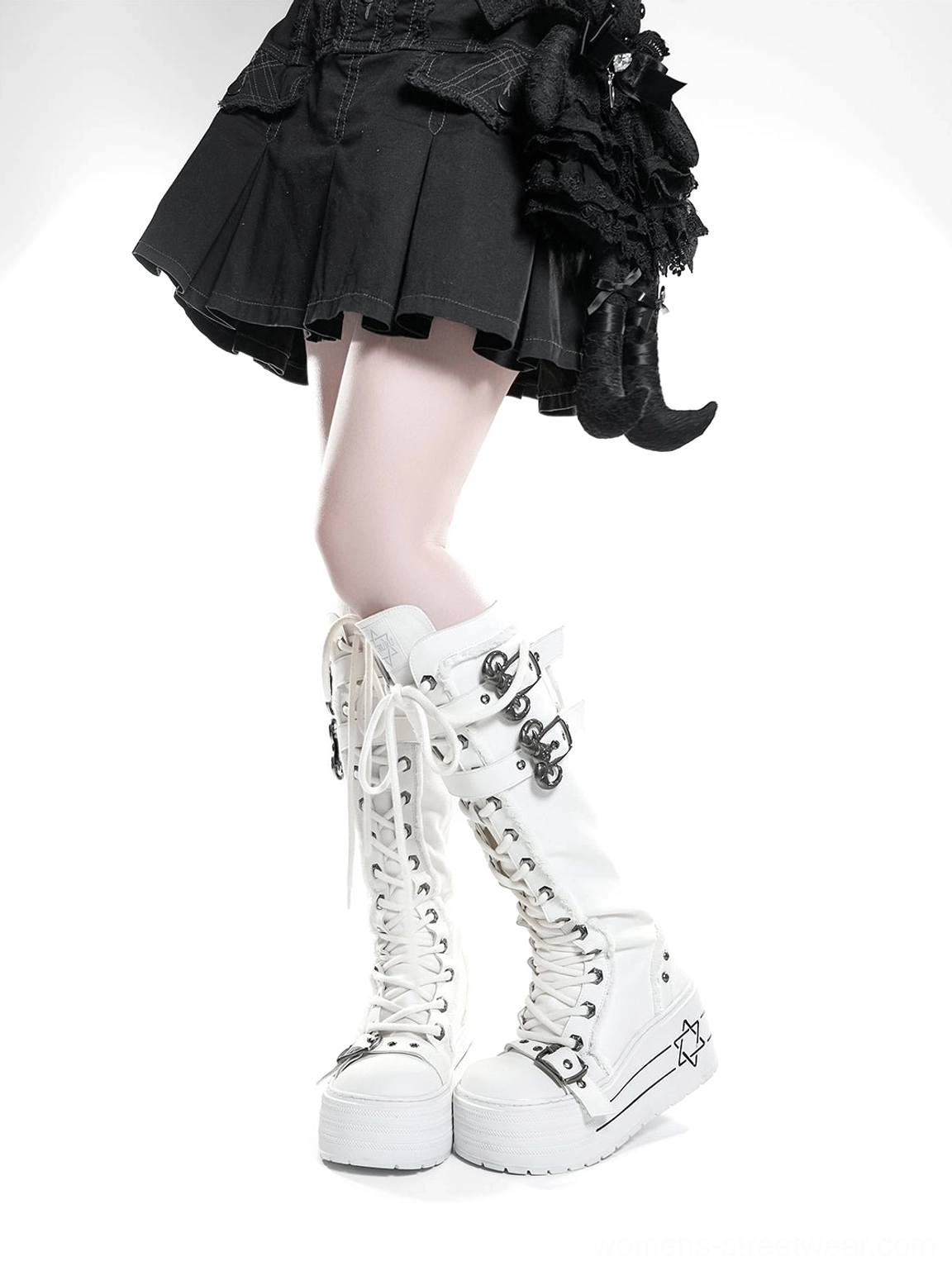 Side profile of white knee-high platform combat boots with metal buckles worn with black pleated gothic skirt