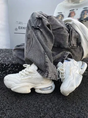 White vortex logo platform sneakers styled with draped denim trousers on urban pavement