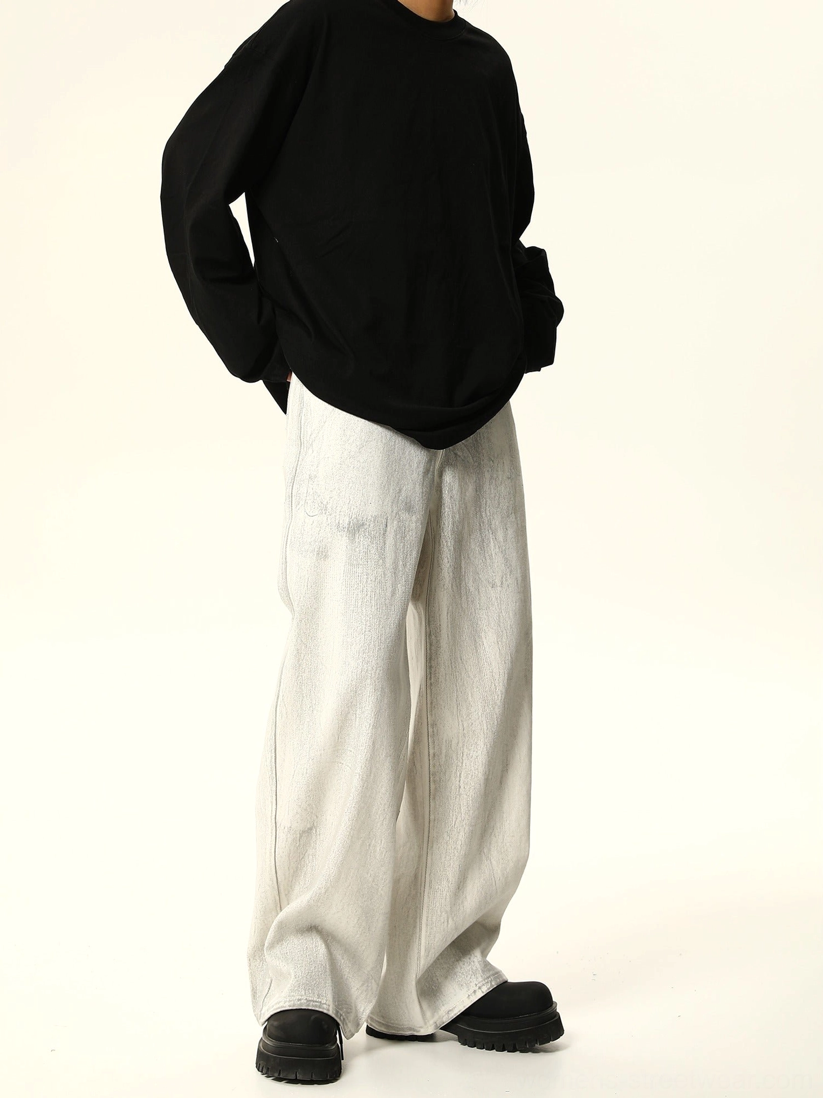 Angled front view of relaxed white washed wide leg jeans styled with an oversized black top and casual black boots