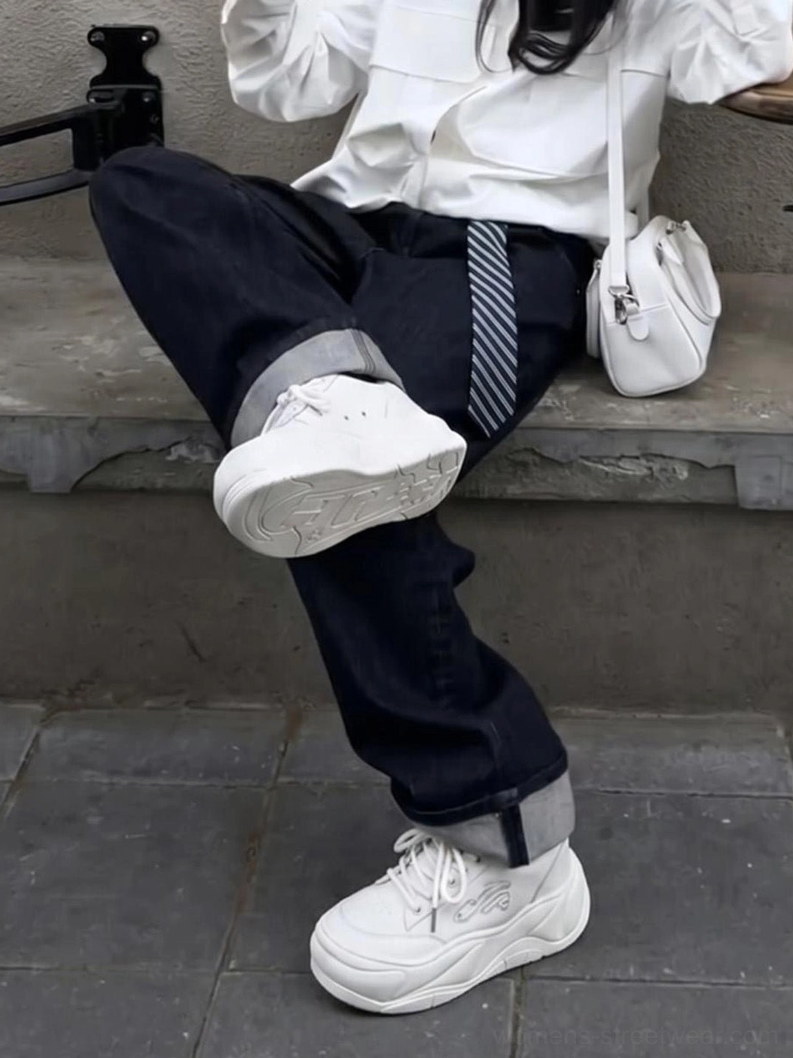 Side view of white wave platform sneakers worn with rolled-cuff dark jeans in a casual city outfit